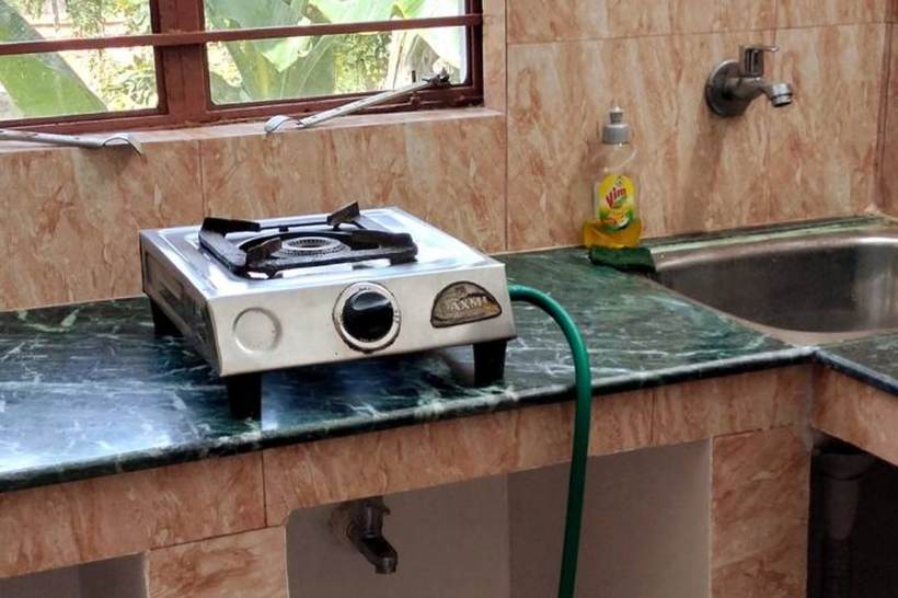 A green marble kitchen counter with a single-burner gas stove, a stainless sink, dish soap and a window looking onto banana leaves.