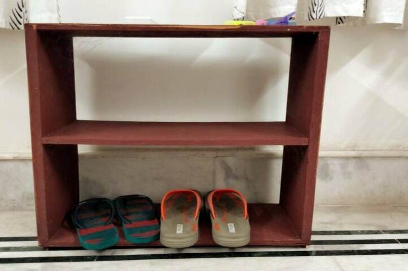 A small dark red wooden shoe rack against a white wall, holding two pairs of rubber slippers.