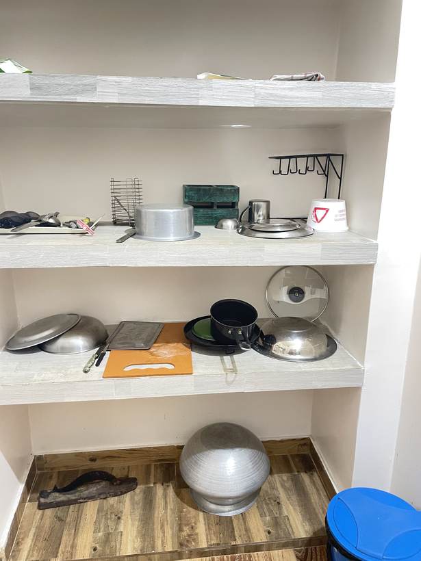 Recessed kitchen shelves holding a karai, lids, a saucepan, a baking tray, a knife and an orange chopping board.