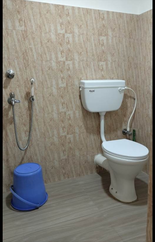 A washroom with beige marbled tiles, a toilet, a health faucet and a blue bucket.