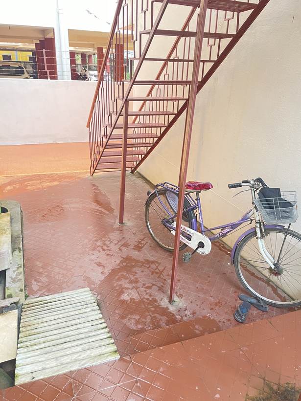 An external red-painted iron staircase against a cream wall, with a purple bicycle parked beneath it on red-oxide tiles.