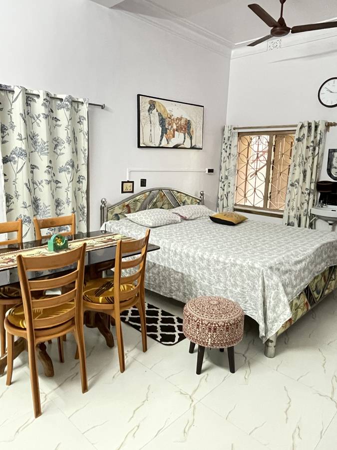 A room with a dining table and four wooden chairs beside the bed, a horse painting on the wall and an iron-grille window.