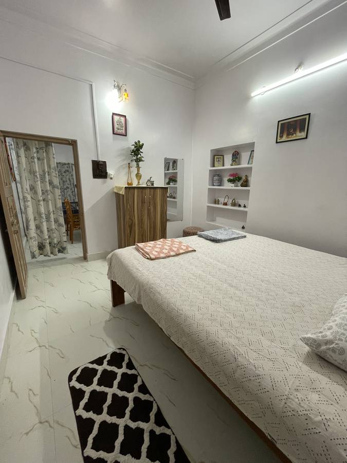 A bedroom with built-in white niche shelves holding brass and terracotta objects, a wooden cupboard and a doorway through to the next room.