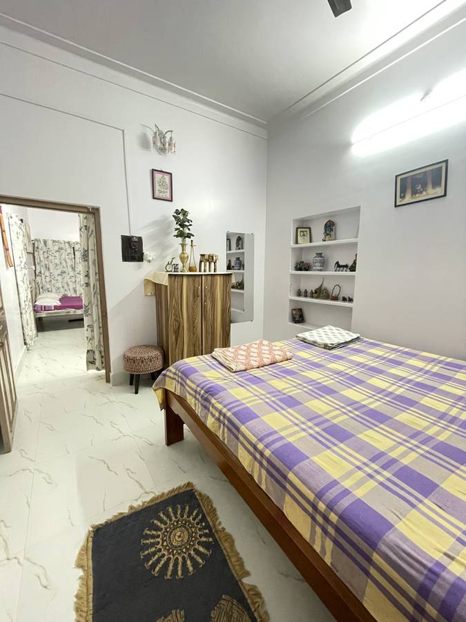 A bedroom with a purple and yellow plaid bedspread and an open doorway showing a second bed in the adjoining room.
